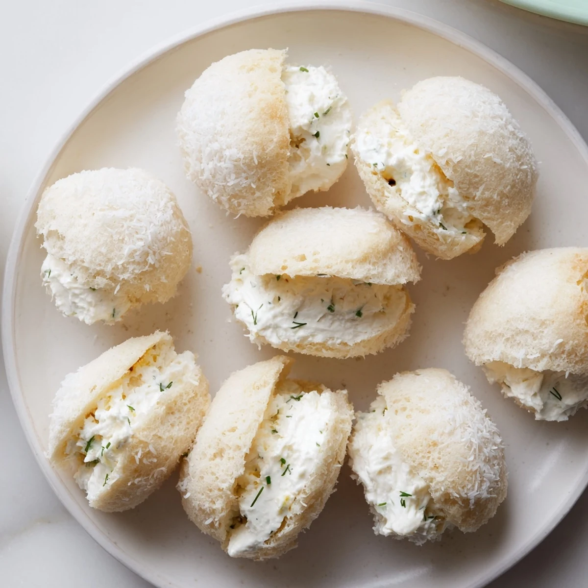 Creamy filling bursting from Snowball Tea Sandwich Bites coated in sweet, shredded coconut for serving.