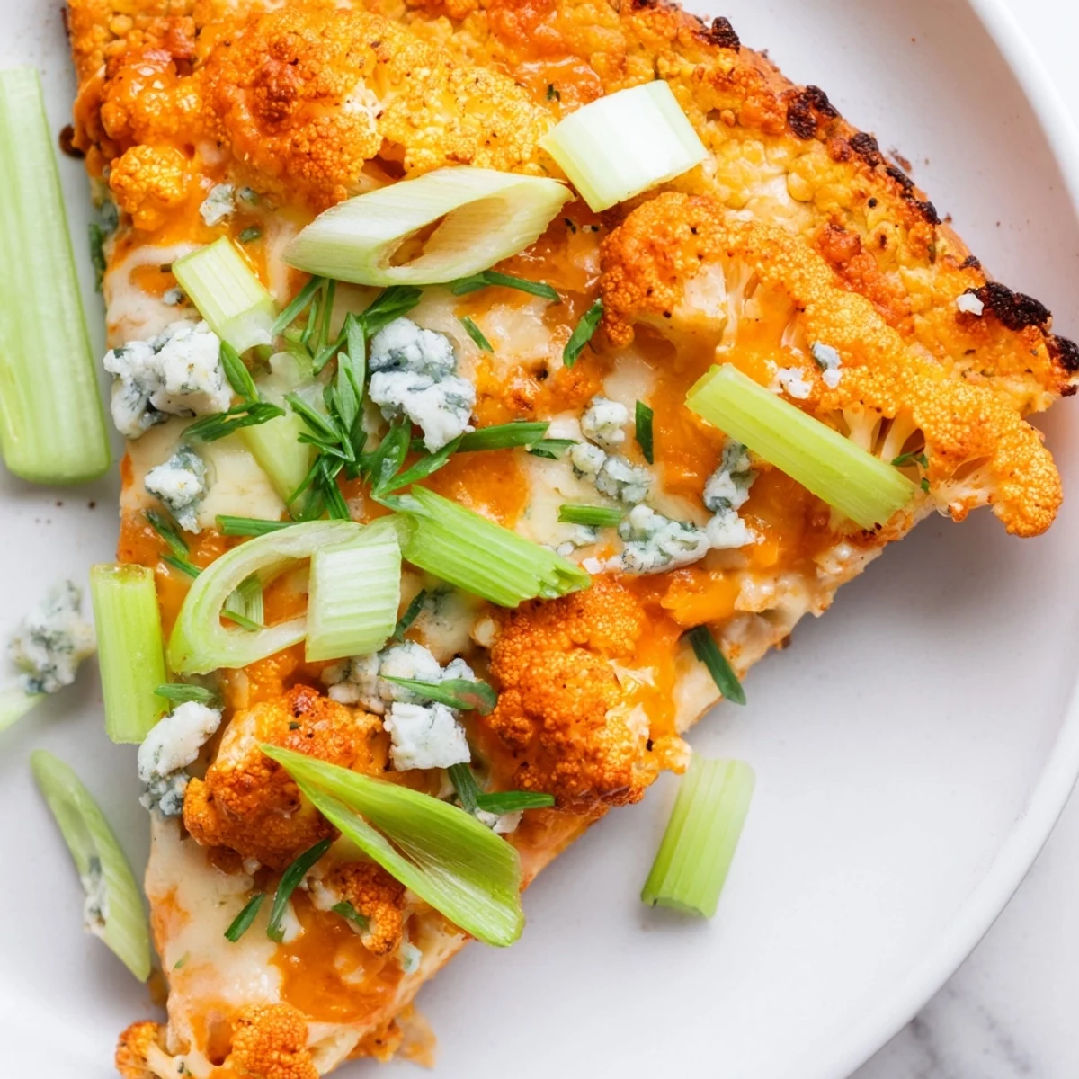 A whole Buffalo Cauliflower Pizza rests on a wooden board, with a side of celery sticks and a glass of milk for serving.