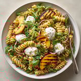 Grilled peach & burrata pasta salad served chilled, featuring creamy cheese and toasty pine nuts.
