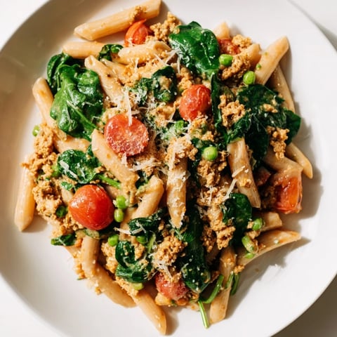One-Pot Creamy Pesto Pea Protein Pasta: a steaming plate of pesto pasta with visible peas and tomatoes.