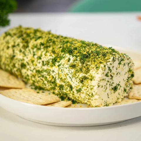 Herb-Coated Cheese Log with vibrant green herbs and a ring of assorted crackers.
