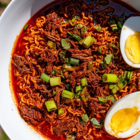 A steaming bowl of flavorful Chaos Cooking Birria Ramen, ready with fresh cilantro and lime.