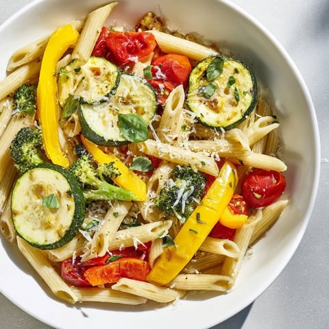 Golden roasted zucchini, yellow squash, and bell peppers tossed with penne pasta, fresh garlic, olive oil, and Parmesan in a vibrant skillet.