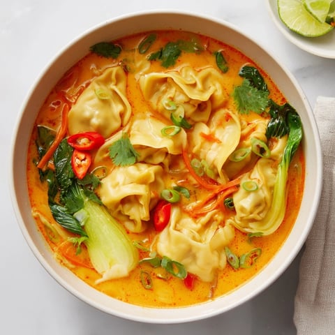 A warm bowl of Red Curry Wonton Soup with Greens featuring plump wontons and fresh spinach in a rich, aromatic broth.  