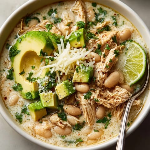 Hearty Budget-Friendly White Chicken Chili with Secret Beans garnished with cilantro and lime wedges for serving.