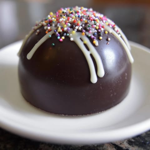 A close-up of a decadent Hot Chocolate Bomb melting in hot milk, ready to drink.