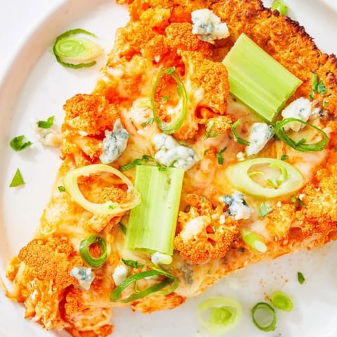 Fresh green onions and sliced celery garnish a slice of Buffalo Cauliflower Pizza, highlighting its vegetarian and gluten-free main dish appeal.