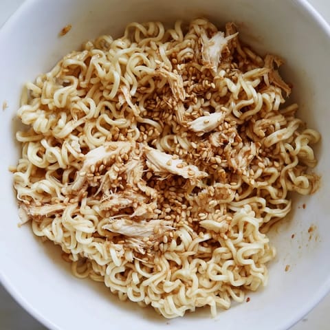 Crunchy Ramen Chicken Salad served in a white bowl with toasted almonds and scallions on a wooden table.