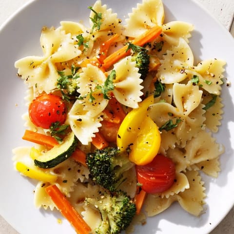 A close-up of a steaming serving of Rainbow Veggie Pasta Primavera, featuring vibrant yellow squash, red bell peppers, and fresh basil leaves on top.