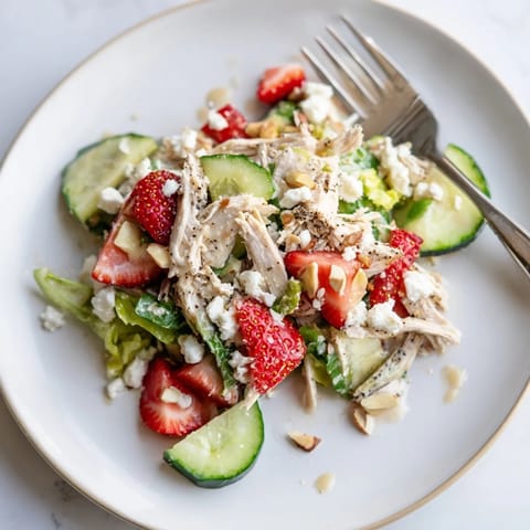 A close-up view of shredded chicken, sliced cucumbers, and feta cheese on salad greens with poppy seed dressing.  